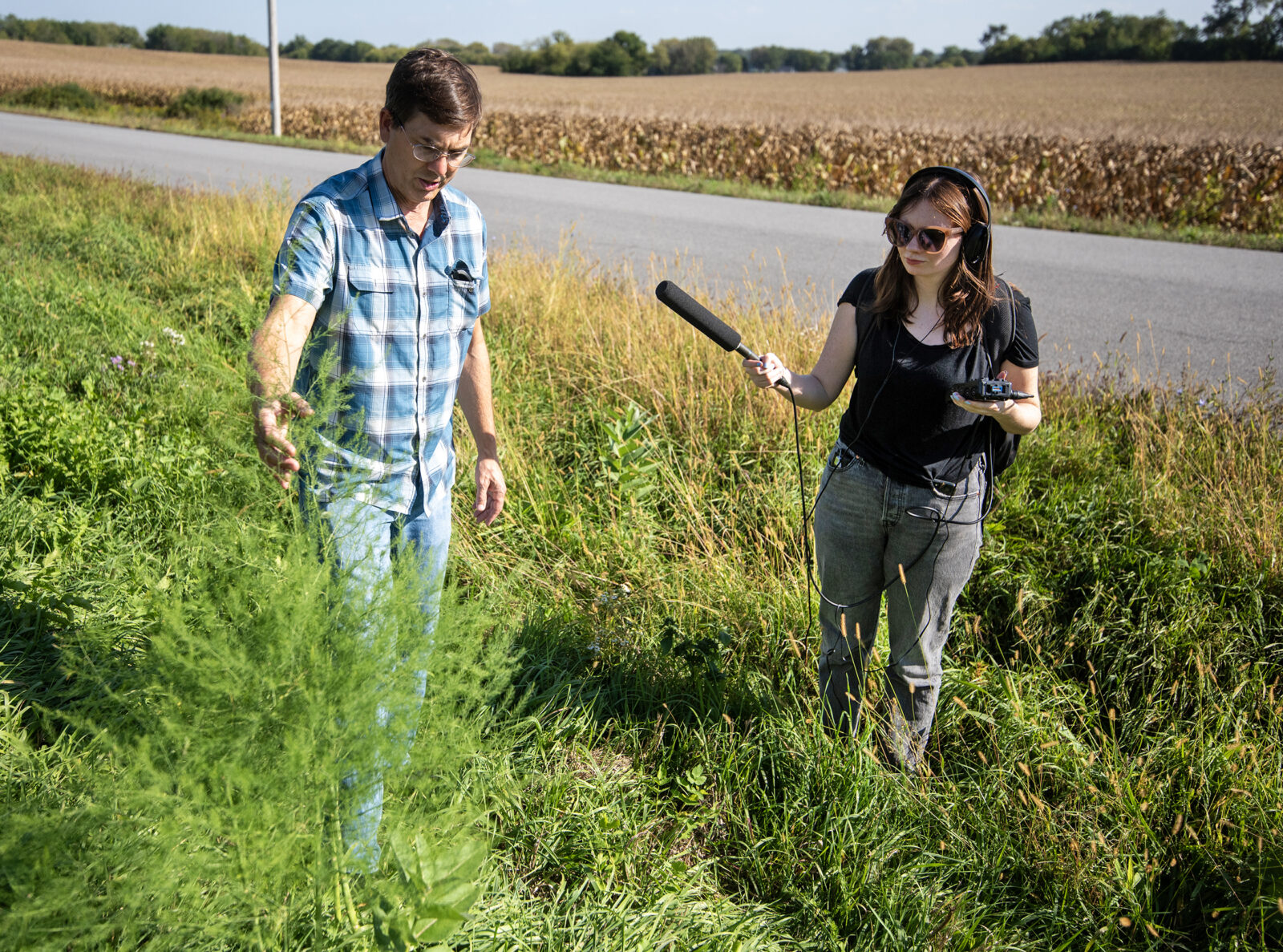 WPR reporter in the field holding a microphone recording an interview with a guest on the side of the road.